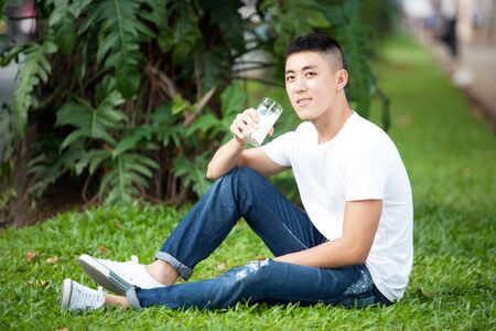 Asian handsome student man drink a glass of milk in the gardenの写真素材