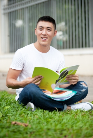 Young handsome Asian student open a book and smile in outdoorの写真素材
