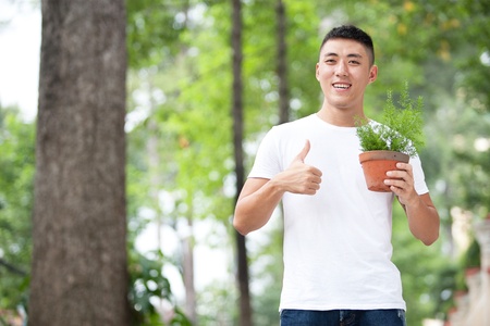 Portrait of young handsome asian student with a plant in clay potの写真素材