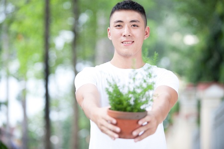 Portrait of young handsome asian student with a plant in clay potの写真素材