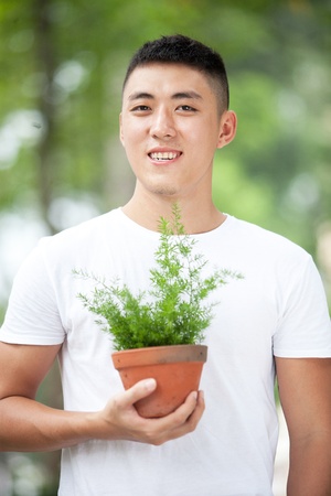 Portrait of young handsome asian student with a plant in clay potの写真素材