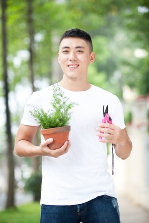 Portrait of young handsome asian student with a plant in clay potの写真素材