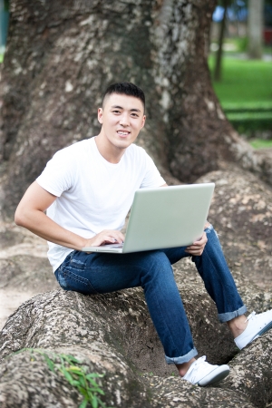 Portrait of young handsome asian student using laptop in the park, smileの写真素材