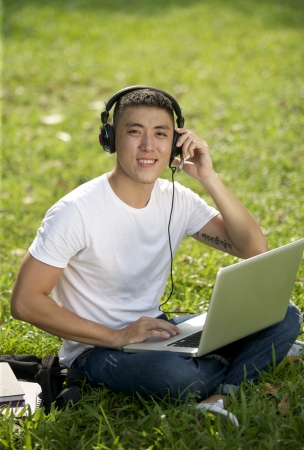 Young handsome Asian student with laptop and headset out doorの写真素材
