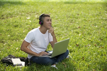 Young handsome Asian student with laptop and headset out doorの写真素材