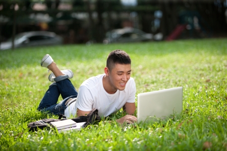 Young handsome Asian student with laptop and headset out doorの写真素材
