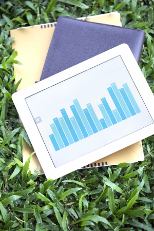 Tablet of business growing chart on grass with booksの写真素材