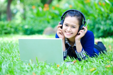 A shot of an Asian college student listening to music lying down on the grass on campusの写真素材