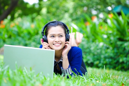 A shot of an Asian college student listening to music lying down on the grass on campusの写真素材