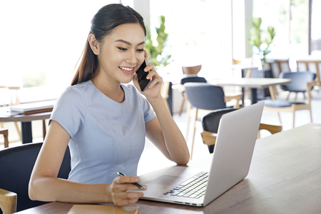 Asian pretty attractive woman working on laptop computer in coffee show with bright optimistic backgroundの写真素材