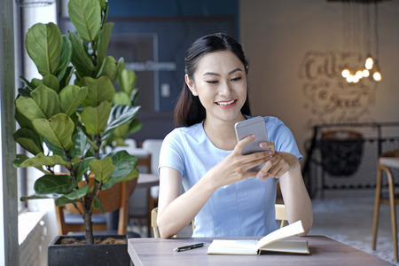 Asian pretty attractive woman sitting in coffee shop using smart phoneの写真素材