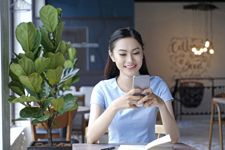 Asian pretty attractive woman sitting in coffee shop using smart phoneの写真素材