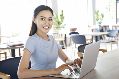 Asian pretty attractive woman working on laptop computer in coffee show with bright optimistic backgroundの写真素材