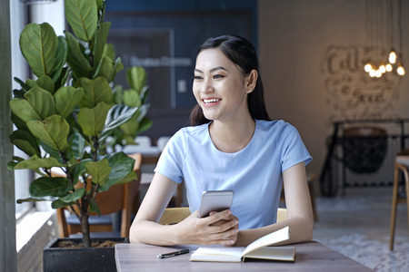 Asian pretty attractive woman sitting in coffee shop using smart phoneの写真素材