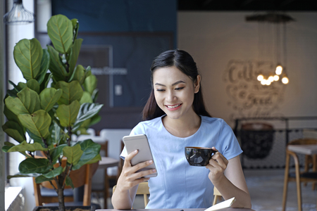 Asian pretty attractive woman sitting in coffee shop using smart phoneの写真素材