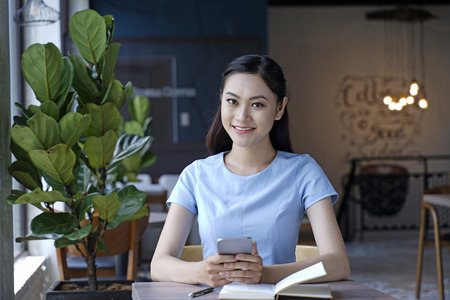 Asian pretty attractive woman sitting in coffee shop using smart phoneの写真素材