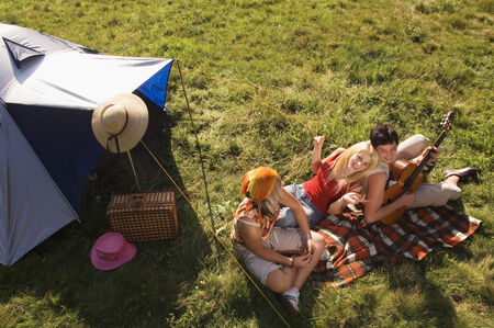 Three young people having picnic, man playing guitar, elevated viewの写真素材