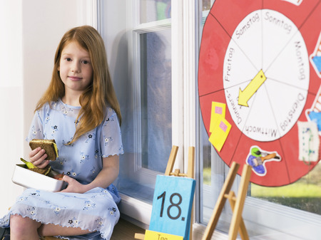 Girl holding lunch box,sitting at classroom windowの写真素材