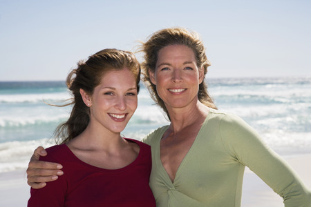 Mother and daughter standing on beach smilingの写真素材