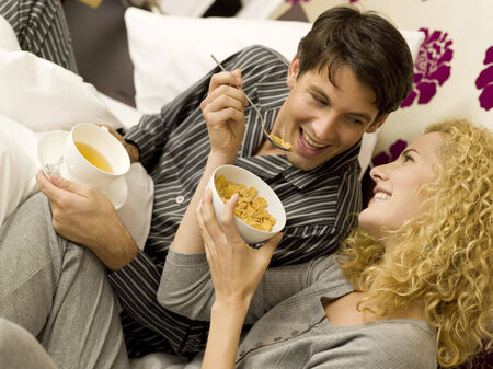 Young couple having breakfast in bed smilingの写真素材