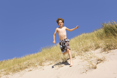Boy running down sand dunes on beachの写真素材