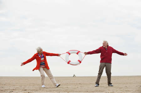 Germany, St Peter-Ording, North Sea, Senior couple pulling lifesaver on beachの写真素材