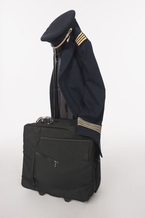 Flight crew uniform and hat hanging on trolley baggage on white backgroundの写真素材
