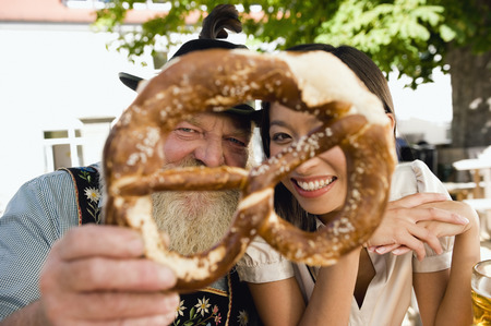 Germany, Bavaria, Upper Bavaria, Bavarian man asian woman holding pretzel looking throughの写真素材