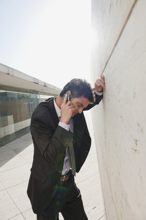 Spain, Mallorca, Businessman using mobile phone, leaning against wallの写真素材