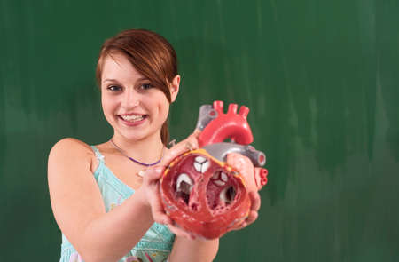 Girl holding artificial heart model chalkboard in background
