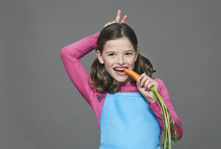 Girl eating carrot gesturing bunny ears behind her own head smiling の写真素材