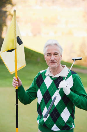 Mature man holding golf club and flagの写真素材