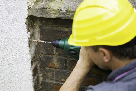 Construction worker using electric drill on brick wallの写真素材