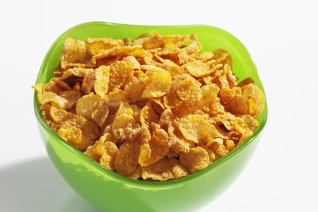 Cornflakes in green plastic bowl on white background