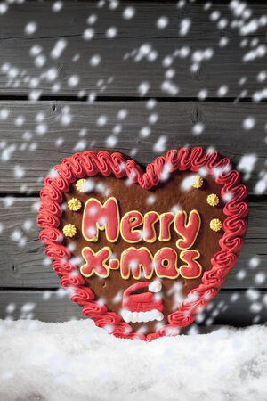 Snowfall with gingerbread heart on heap of snow against wooden backgroundの写真素材
