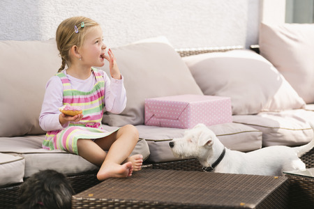 Young girl eating doughnut dog waiting next to herの写真素材