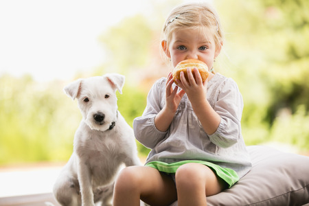 Young girl sitting on wooden steps with her dog eating doughnutの写真素材