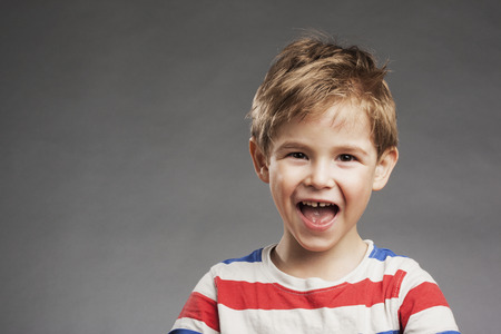 Young boy laughing against gray background, portraitの写真素材