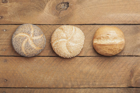 Wheat roll, poppy seed roll and sesame roll on wood