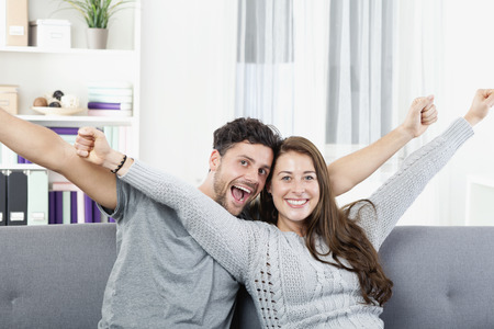 Cheerful young couple sitting on sofa, arms outの写真素材
