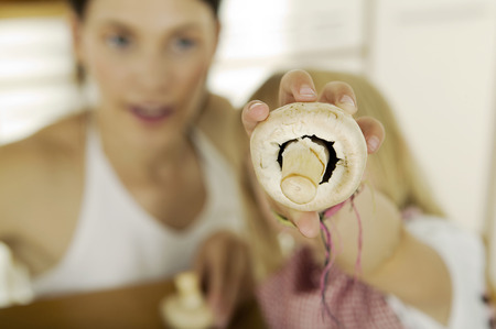 Little girl (4-5) holding mushroom,mushrooms, mother in backgroundの写真素材