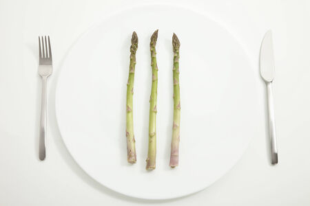 Asparagus in plate with fork and knife on white backgroundの写真素材
