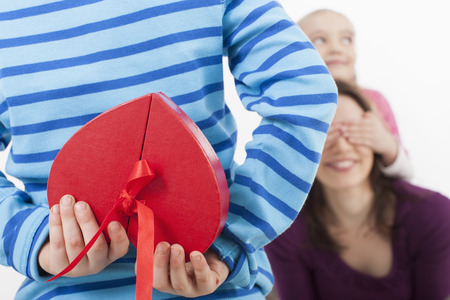 Daughter covering eyes of mother, Son with gift box in foregroundの写真素材
