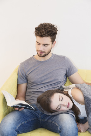 Young couple resting on sofa, he reading a bookの写真素材