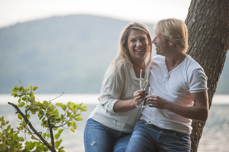 Happy couple with champagne glasses at lakeの写真素材