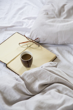 Coffee cup, book, reading glasses on bedの写真素材