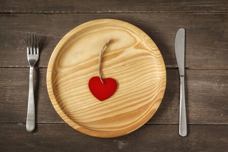 Wooden plate with heart, knife and fork on woodの写真素材