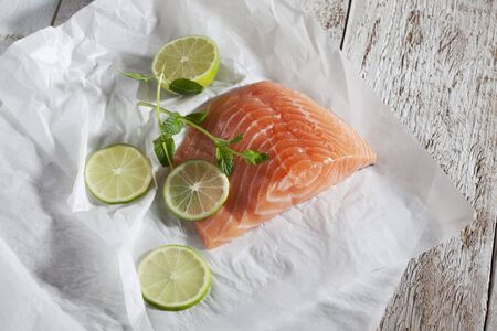 Fish fillet, salmon, limes and herbs on greaseproof paper, woodの写真素材
