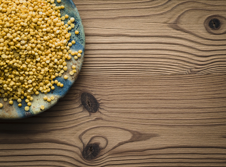 Yellow lentils on plate against wooden background