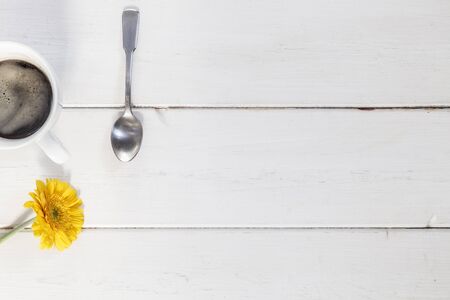 Cup of coffee and yellow gerbera on white wood
